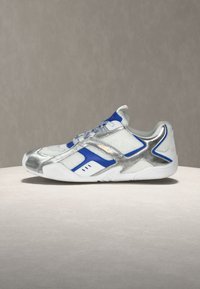 Baskets basses blanches et bleues avec des accents métalliques argentés et une semelle blanche, montrées de profil sur un fond neutre.