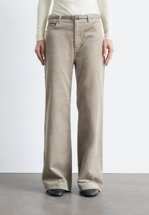 Beige corduroy wide-leg trousers with a textured finish, featuring a fitted belt and front pockets, paired with black footwear.