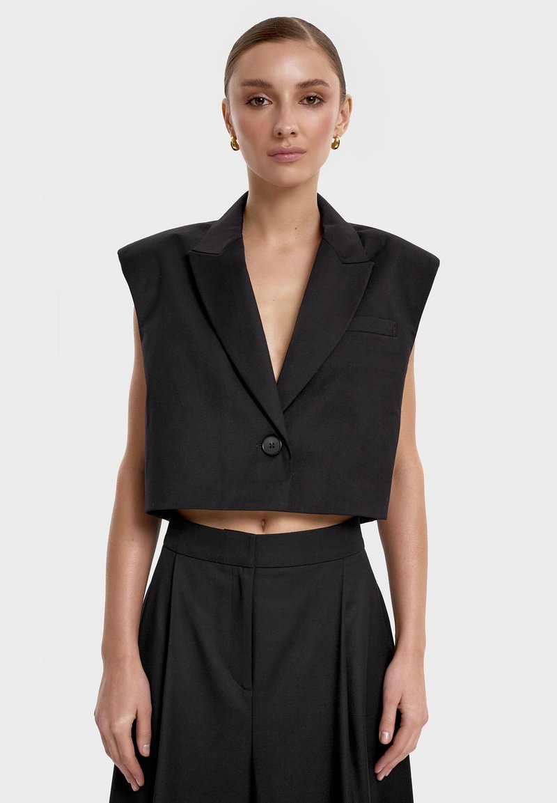 Czarna krótka marynarka z poduszkami na ramionach, zapięcie na jeden guzik, kołnierz klapowy oraz przednia kieszeń. Gładka tekstura i dopasowany krój.