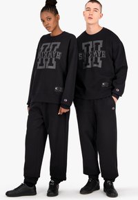 Las sudaderas y pantalones de algodón negro presentan un llamativo logo "HAWKINS" en gris, con acentos logo, un corte relajado y puños acanalados.