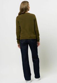 Olivgrön tröja med rund halsringning och ribbad struktur, kombinerad med mörkblå raka jeans och vita sneakers.