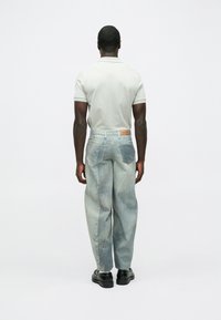 Svijetlosiva polo majica uparena s velikim trapericama plavkaste nijanse koje imaju teksturirani uzorak i kožnu oznaku s logom na pojasu.