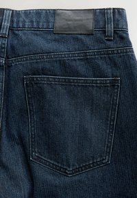 Tumedast sinine denim, millel on voolujooneline disain, tagakotiga ja mustast nahast vöö silt. Tekstureeritud kangas peenete õmblustega.