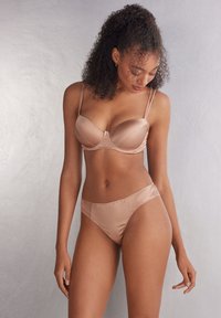 Sukienka bra wykonana z satyny oraz pasujące majtki o wysokim stanie w kolorze nude. Biustonosz posiada fiszbiny oraz regulowane ramiączka; majtki są gładkie z elastyczną talią.