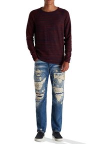 Maglietta a maniche lunghe color bordeaux con trama testurizzata, abbinata a jeans strappati blu con grandi strappi e un accento blu. Sneakers nere completano il look.
