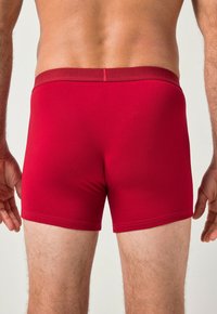 Bóxer de algodón rojo con una textura suave y cinturilla elástica. Visto desde la parte posterior, mostrando un diseño ajustado y detalles de costura mínimos.