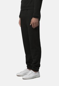 Pantaloni della tuta neri con polsini in elastico, in misto cotone, dotati di tasche laterali, abbinati a sneakers bianche con superficie testurizzata.