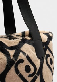 Borsa in pelliccia sintetica beige e nera con motivo astratto a spirale e manici in pelle nera, mostrata in primo piano su sfondo bianco.