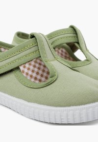 Las zapatillas de lienzo verdes cuentan con un diseño de correa en T, suela de goma blanca y un forro de patrones de cuadros. Textura suave con costuras reforzadas.