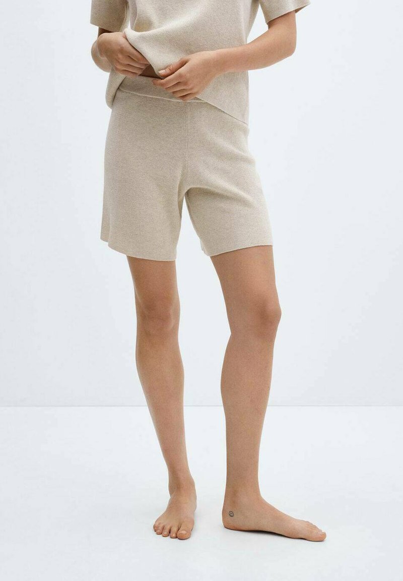 Beige strikket lounge-sæt bestående af en kortærmet top og shorts til midt på låret. Stoffet har en glat tekstur og en tætsiddende pasform.