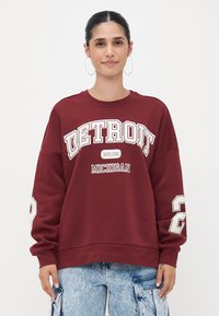 Sweatshirt bordeaux com gráficos em branco de "DETROIT" e "MICHIGAN", corte oversized, punhos canelados e um grande número "2" na manga.