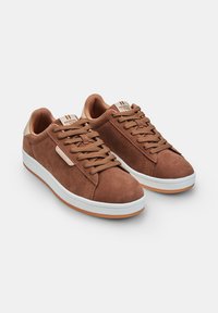 Sneaker basse in suede marrone con punte tonde, design con lacci, suole in gomma bianca e brand sul tallone. Superfici lisce e testurizzate.