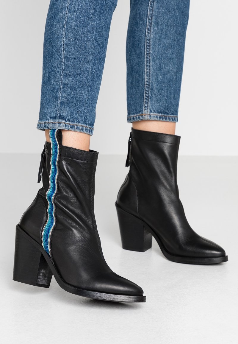 Bottes courtes en cuir noir avec un bout pointu et un talon bloc. Présentent un accent côtelé turquoise et bleu le long de la fermeture éclair latérale.
