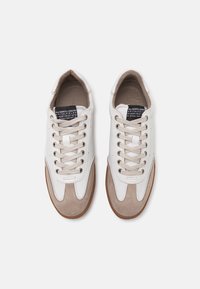Hvite sneakers med beigefargede suede-detaljer, flate lisser og en teksturert gummisåle. Har merke-tags innvendig i skoen.
