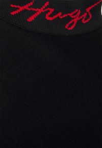 Prenda negra con una superficie texturizada y un cuello acanalado, con texto rojo bordado a lo largo del borde, que presenta un diseño minimalista.