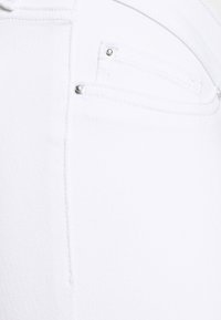 Valkoinen denimp ткань с нежной текстурой. Имеет задний карман с серебряной фурнитурой и чистый, минималистичный дизайн.