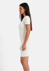 Weißes, figurbetontes, geripptes Kleid mit kurzen Ärmeln. Der Stoff hat ein strukturiertes Muster. Das Kleid endet über dem Knie und zeigt eine elegante Silhouette.