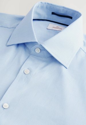 Cămașă texturată de un albastru deschis, cu guler larg, două butoane albe și o etichetă care spune "NEXT SIGNATURE". Materialul pare moale și respirabil.