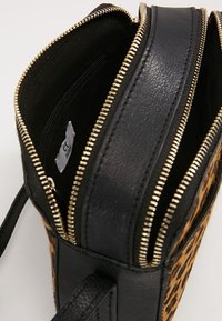 Taske med leopardprint, der har sort læderkant, gyldent lynlås og inderlomme med lynlås. Struktureret design med to lommer med lynlås.