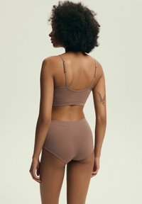 Brązowy stanik typu bralette z regulowanymi ramiączkami w połączeniu z wysokim stanem majtek, prezentujący miękki, elastyczny materiał i minimalistyczny design.