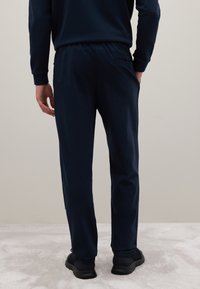 Pantaloni sportivi blu navy con vita elasticizzata e tasche laterali, caratterizzati da una texture liscia e un design affusolato, visti da dietro.
