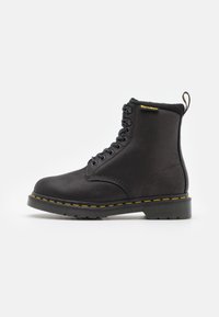 Botín negro de piel con diseño de cordones, punta redonda, costuras amarillas y suela de goma texturizada. Presenta un cuello suave y una lengüeta.