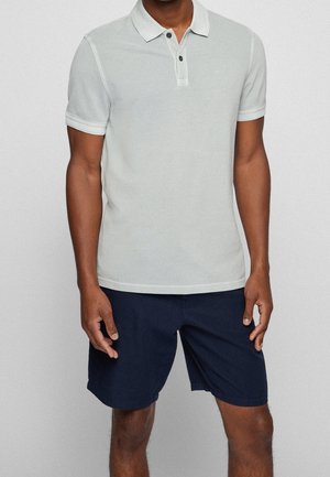 Jasnoszara koszulka polo o miękkiej fakturze, z trzema guzikami i kontrastującym kołnierzykiem; w zestawie z ciemnogranatowymi szortami.
