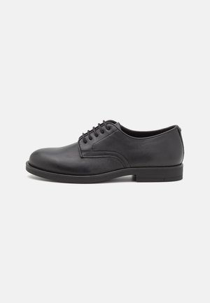 Zapato formal de hombre de cuero negro con cordones, puntera redondeada y tacón bajo, mostrado de perfil sobre un fondo liso.