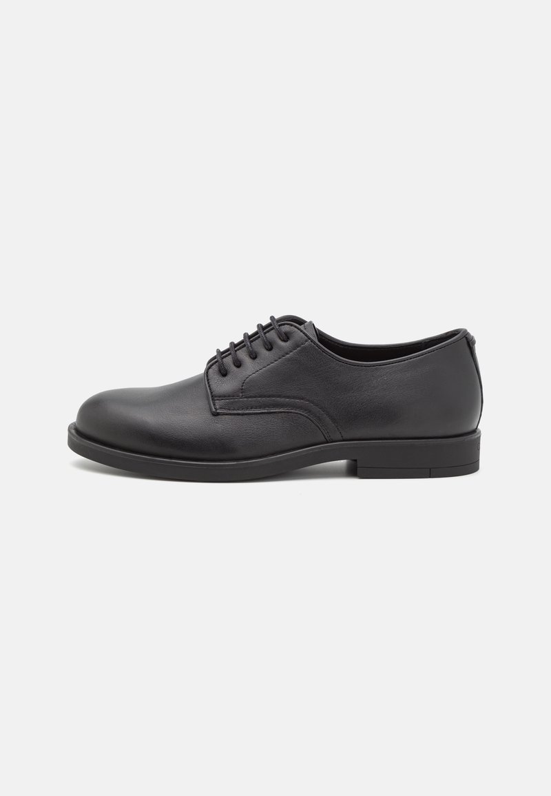 Chaussure habillée en cuir noir pour homme, à lacets, avec un bout rond et un petit talon, vue de profil sur un fond uni.
