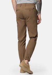 Brązowe bawełniane spodnie o slim fit, z tylnymi kieszeniami i podwiniętymi mankietami. Noszone z beżowymi zamszowymi sneakersami dla spójnego wyglądu.