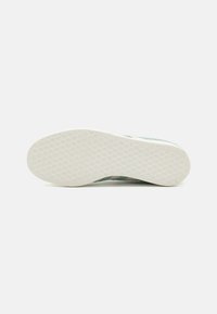 Suela de zapatilla con una parte inferior de goma blanca texturizada, que presenta un patrón hexagonal y acentos en verde claro en los lados.