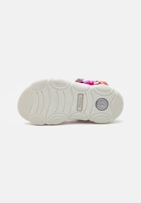 Hvit sneakersåle med teksturert gummi, buede spor og et sirkulært logo. Fargerik overdel vist delvis med rosa, lilla og oransje detaljer.