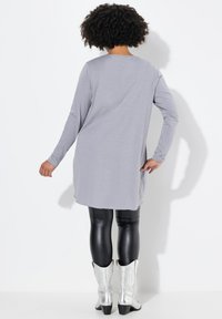 Graues Langarm-Tunika-Shirt mit lockerer Passform, kombiniert mit schwarzen Leggings aus Kunstleder und silbernen Ankle Boots im Western-Stil.