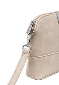 Beige kabelka vyrobená z texturovaného syntetického materiálu. Má zipové uzavření, kovové detaily a odnímatelný popruh se švy.