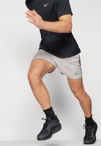 Grey athletic shorts and a black Nike t-shirt are worn with black sneakers and socks. The figure is in a running pose.