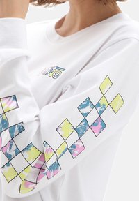 Camisa blanca de manga larga con un patrón geométrico multicolor en las mangas y un pequeño gráfico de logo en la parte frontal. Material de algodón.