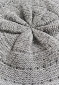 Gorro gris de punto con un patrón en espiral, tejido texturizado y un acabado suave y peludo. El detalle central muestra secciones de tela retorcidas.