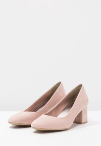 Scarpe con tacco alto in suede rosa, con punta squadrata, tacco a blocco e una superficie liscia. L'interno presenta una fodera di colore chiaro.