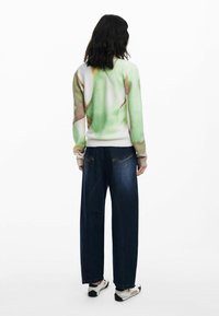 Trui in groen en roomwitte kleuren met abstracte patronen, gecombineerd met wijde, donkerblauwe jeans. Zachte stof, geribde mouwen en tailleband.