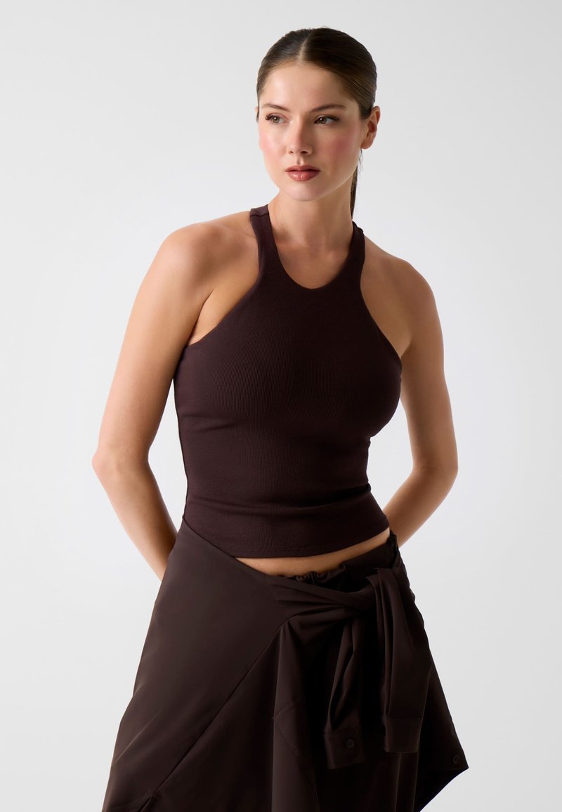 Haut marron côtelé à col licou avec une coupe ajustée. L'encolure présente une coupe arrondie. Porté avec une jupe portefeuille marron assortie.