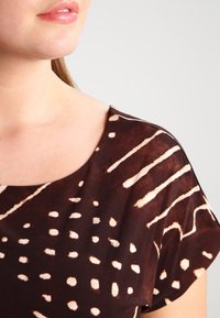 Brun tygöverdel med rund halsringning som har ett mönster av vita prickar och ränder. Mjuk textur, korta ärmar och avslappnad passform.