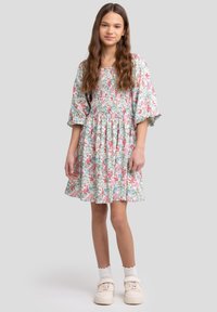 Blomstret kjole med korte puffærmer, indsamlet talje og knælang nederdel. Lys blå baggrund med pink og grønne blomster. Hvide sneakers.