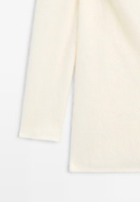 Blød cremefarvet sweater med en afslappet pasform, lange ærmer og en glat, struktureret overflade. Enkel design uden synligt hardware eller mønstre.