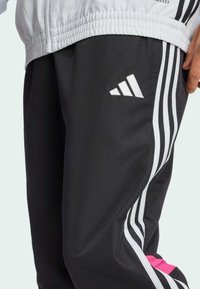 Schwarze Sporthose mit einem weißen Drei-Streifen-Design und pinken Akzenten. Hergestellt aus glattem Stoff, mit einem gestickten Logo am Oberschenkel.