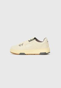 Zapatillas hechas de malla beige y material sintético, con un acento gris, suela texturizada y un logotipo sutil en el talón.