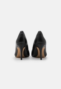 Chaussures à talons hauts en cuir noir avec un bout pointu et un talon aiguille fin, présentant une texture lisse et un design minimaliste.