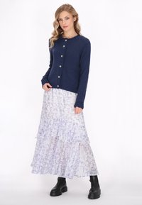 Navy knitted cardigan with scalloped collar and silver buttons, paired with a tiered, floral-patterned maxi skirt in pastel shades and black ankle boots.