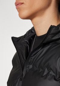 Černá péřová bunda s vysokým límcem, lehkým materiálem a zapínáním na zip. Texturovaný povrch s viditelnými detaily prošití.