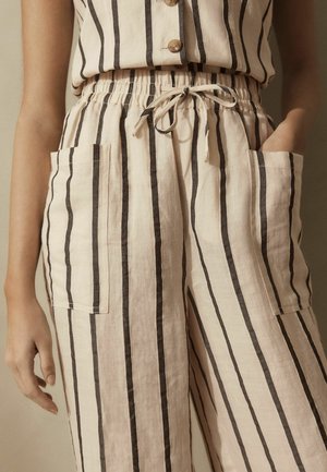 Pantalons en lin légers avec des rayures noires verticales sur un fond beige, dotés d'une taille élastique, d'un cordon de serrage et de poches latérales.