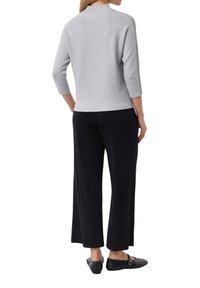 Grijze, geribbelde trui met hoge hals, gecombineerd met zwarte wijde broek en zwarte flats, gezien vanaf de achterkant.